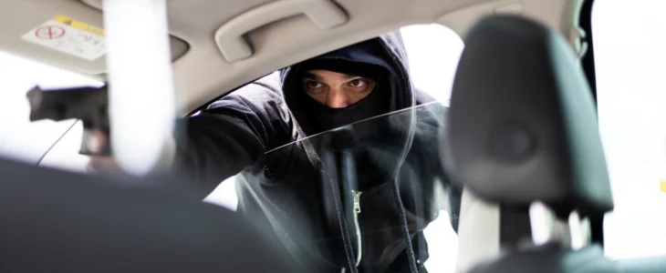 Man in black mask with a gun carjacking a vehicle