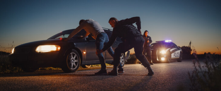 Policeman searching male suspect outside of a vehicle