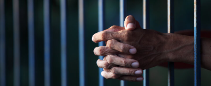 Man's hands resting through jail cell bars