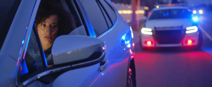 A young multiracial woman in a car, pulled over by a police officer at night.