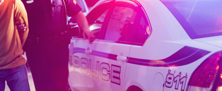 Police officer making an arrest, escorting a young man in handcuffs toward the back seat of his police car