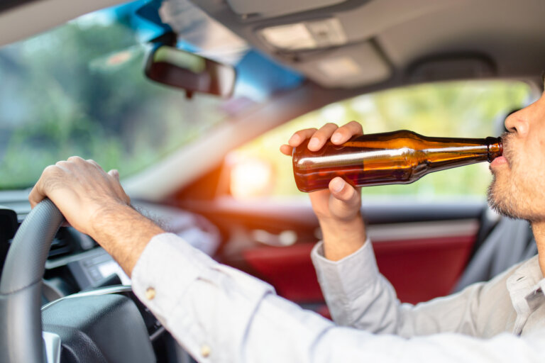 Drunk asian young man drives a car with a bottle of beer with sunset background, Dangerous driving concept