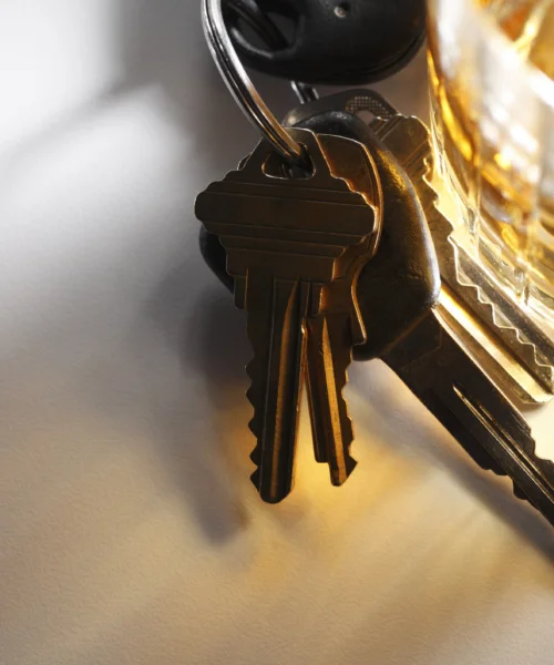 A set of keys resting next to a glass of alcohol
