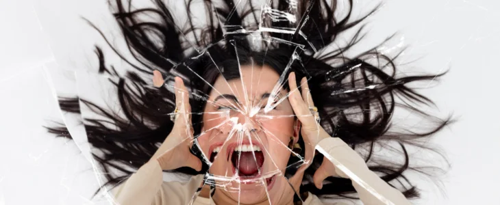 Woman screaming with her hands either side of her head with a cracked mirror effect over the image.