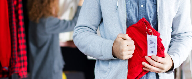 Closeup of young man is stealing red jeans in store, shop, boutique at shopping center.