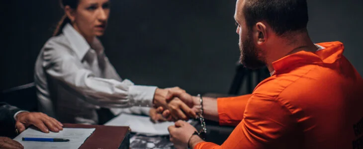 prisoner in dark investigation room, shaking hand with lawyer.