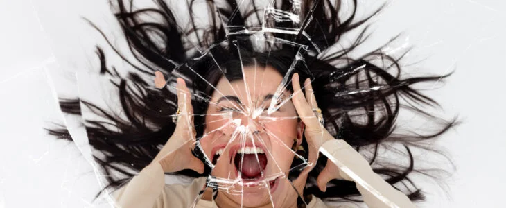 Woman screaming with her hands either side of her head with a cracked mirror effect over the image.